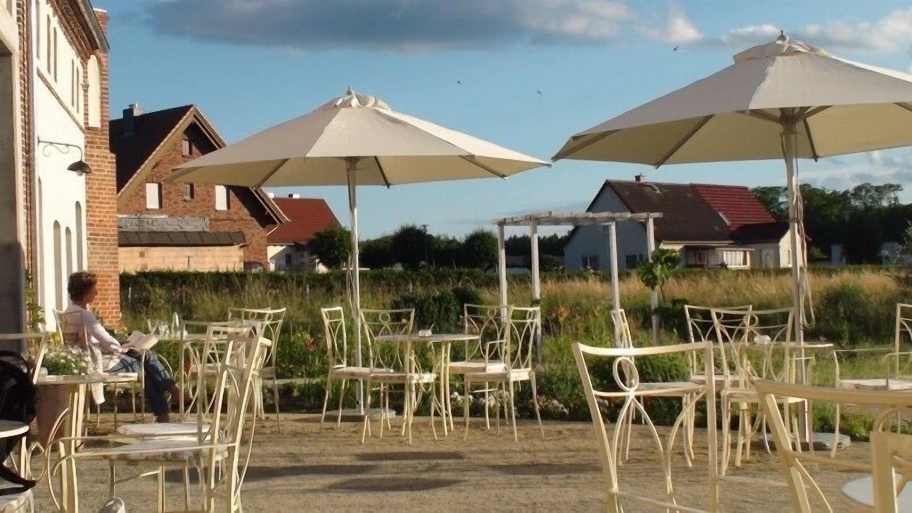 An outdoor patio with tables and chairs, umbrellas, and a person sitting at a table.