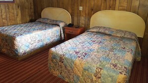 Una habitación con dos camas individuales, paneles de madera en las paredes, una mesita con una lámpara y cuadros enmarcados.