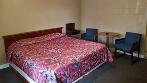 Habitación de hotel con cama, dos sillas, una mesita y un teléfono en la mesita de noche.