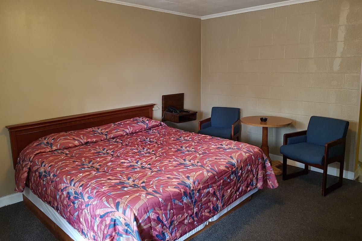 Hotellihuone, jossa on sänky, kaksi tuolia, pieni pöytä ja puhelin yöpöydällä.