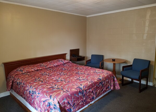 A hotel room with a bed, two chairs, a small table, and a phone on a nightstand.