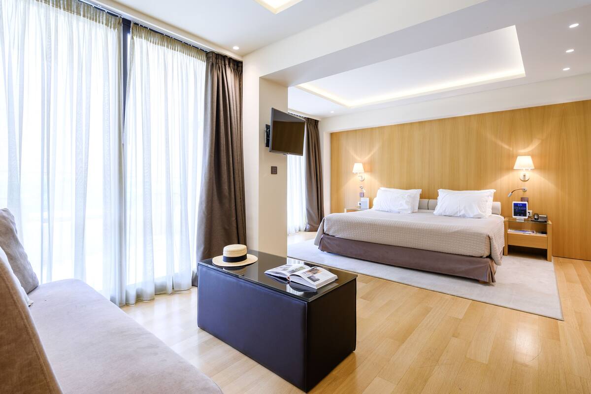 Una habitación de hotel moderna con cama, sofá, mesa de centro y televisión.