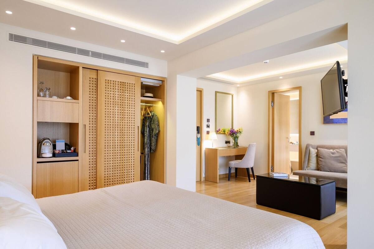 A hotel room with a bed, a desk, a chair, a sofa, a TV, and a wardrobe.