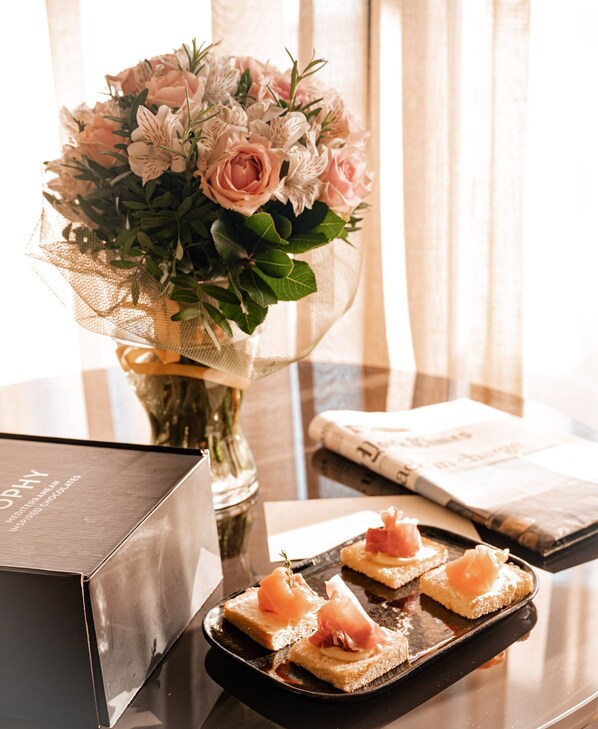 A table with a bouquet of flowers, a box, and a tray of food. - Somewhere Boutique Hotel Vouliagmeni (Vari-Voula-Vouliagmeni)