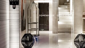 Een moderne hotellobby met een glazen ingang, een receptiebalie en een trap naar de verdiepingen erboven.