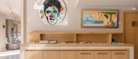 A reception desk with a wooden finish, a large abstract painting, and a framed artwork above it.