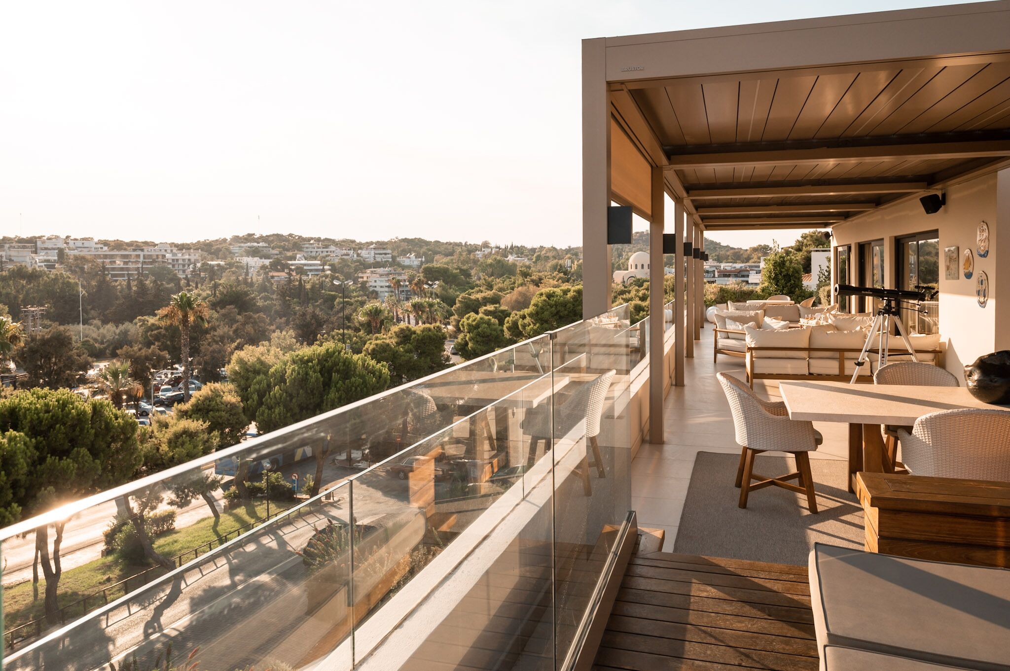Ein moderner Balkon mit Glasgeländer, Holzdeck und einer Sitzecke mit weißem Rattanmöbeln.