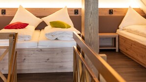 Una habitació acollidora i ben il·luminada amb terra de fusta, un llit amb roba de llit i almoadines blancs, i una petita taula de nit.
