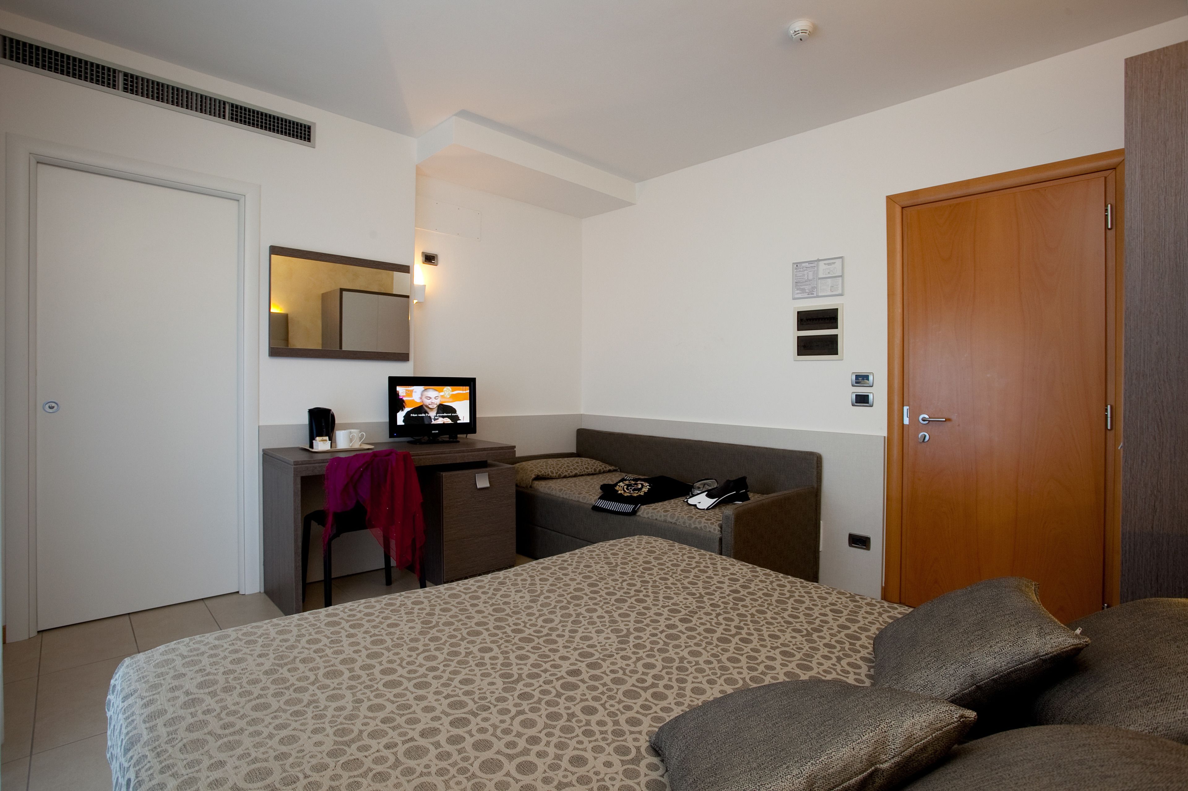 Una habitación de hotel con una cama, un escritorio con computadora, una silla, un sofá y una puerta de madera.