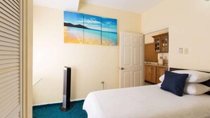 Een hotelkamer met een bed, een schilderij van een strandzicht, een deur en een kitchenette.