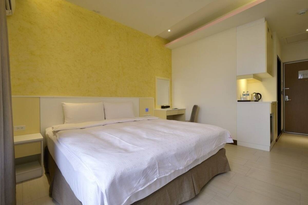 A hotel room with a large bed, a desk with a chair, and a kitchenette area.