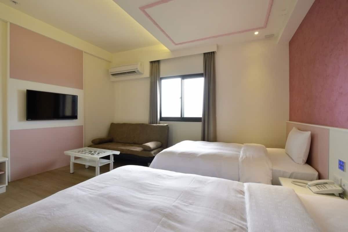 A hotel room with two beds, a sofa, a TV, and a window with curtains.