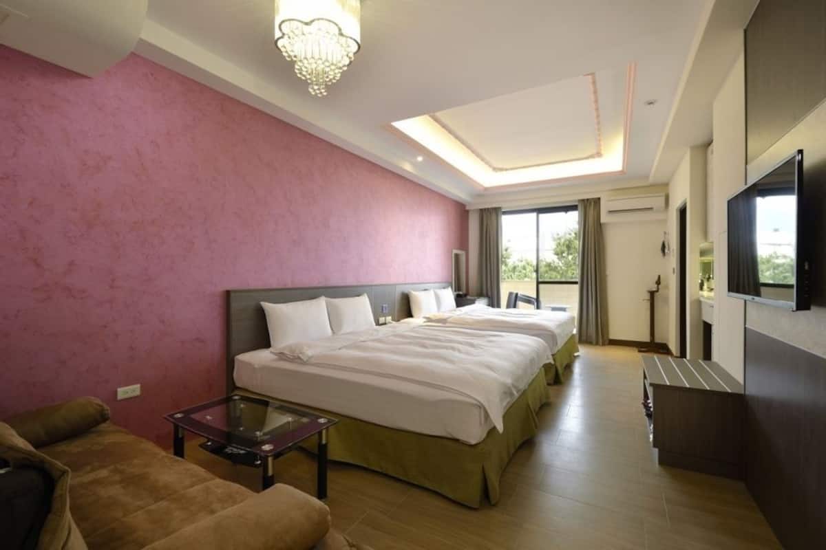A hotel room with two beds, a sofa, a TV, and a balcony with a view.