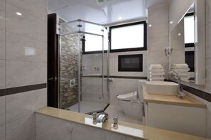 Un baño moderno con ducha envuelta en vidrio, lavamanos con espejo y ventana que proporciona luz natural.