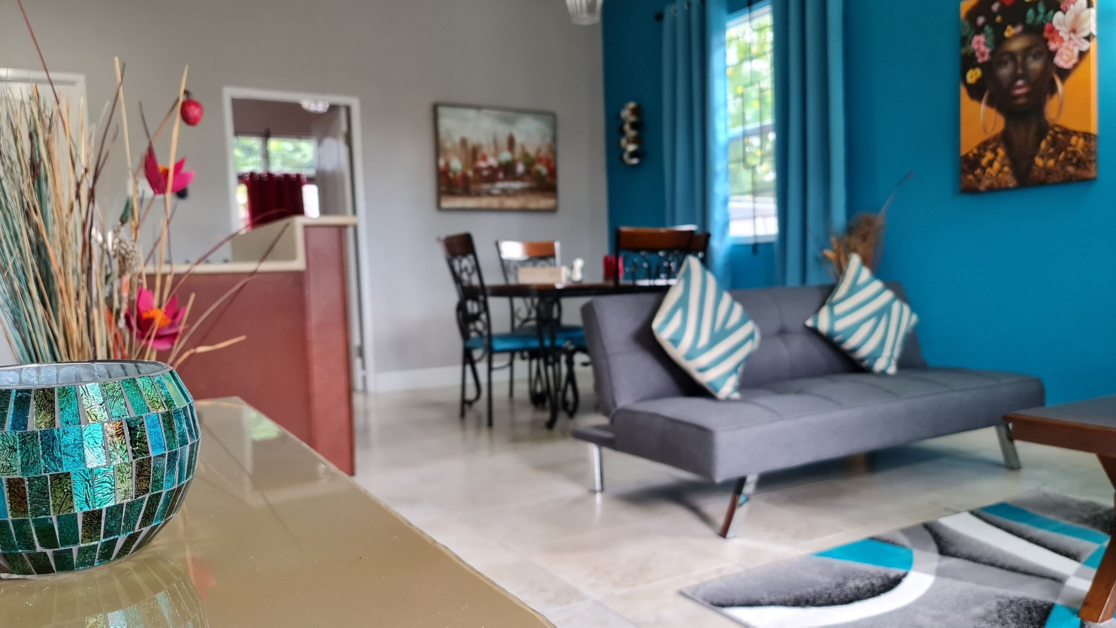 A modern living room with a grey sofa, a dining table with chairs, and a kitchen area in the background.