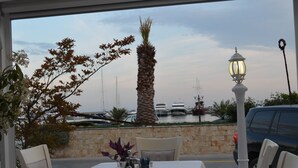 Un espacio exterior para comer con una mesa dispuesta para dos, con vistas a un puerto deportivo con barcos y una palmera.