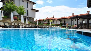 Una piscina con sillas de descanso y sombrillas, rodeada de edificios con techos de tejas rojas.