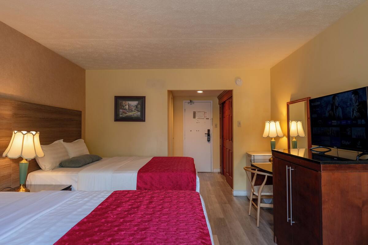 Una habitación de hotel con dos camas, un escritorio, una silla, un televisor y un espejo.