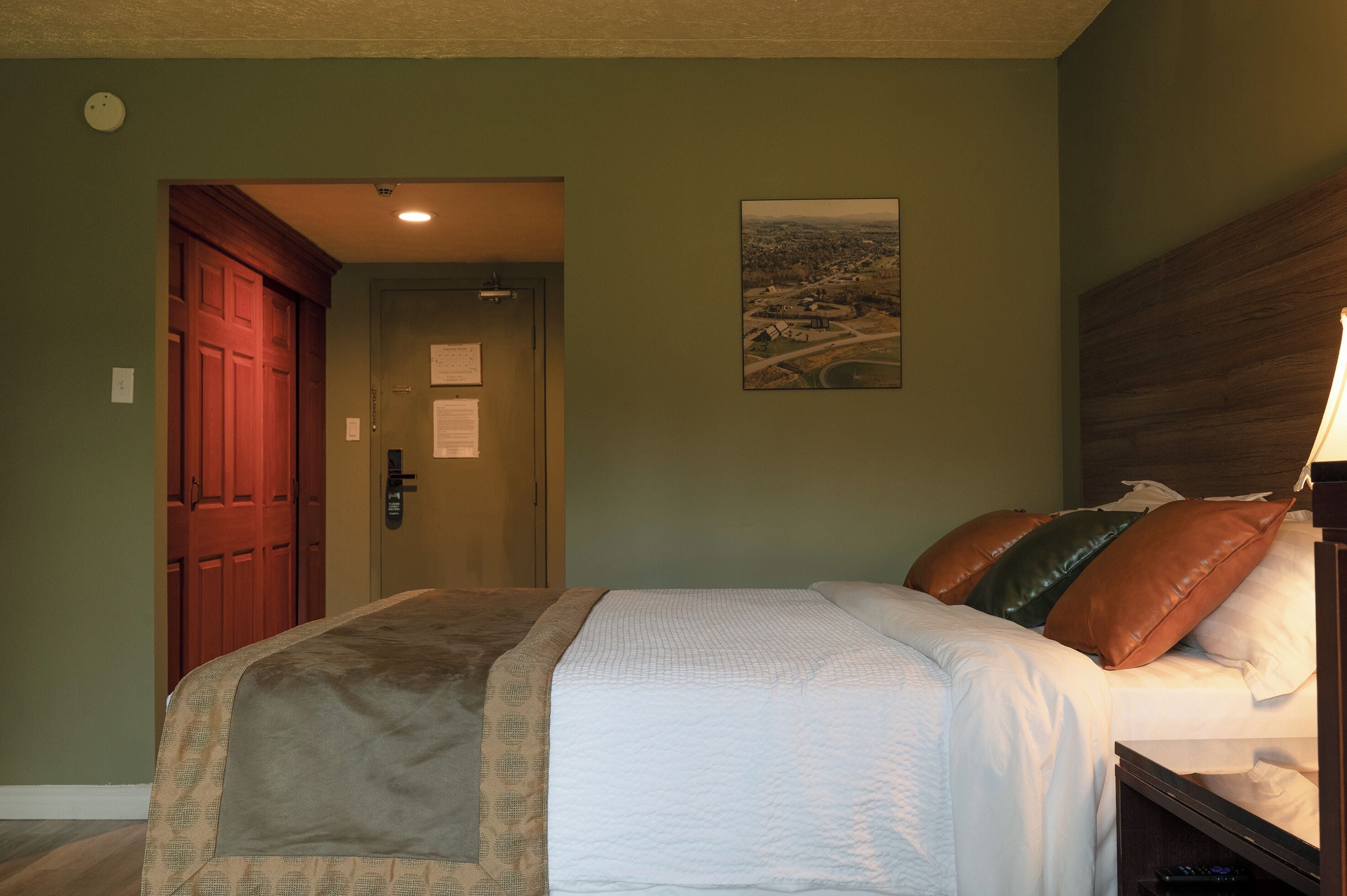 A bedroom with a bed, a wooden door, a view poster, and a nightstand.