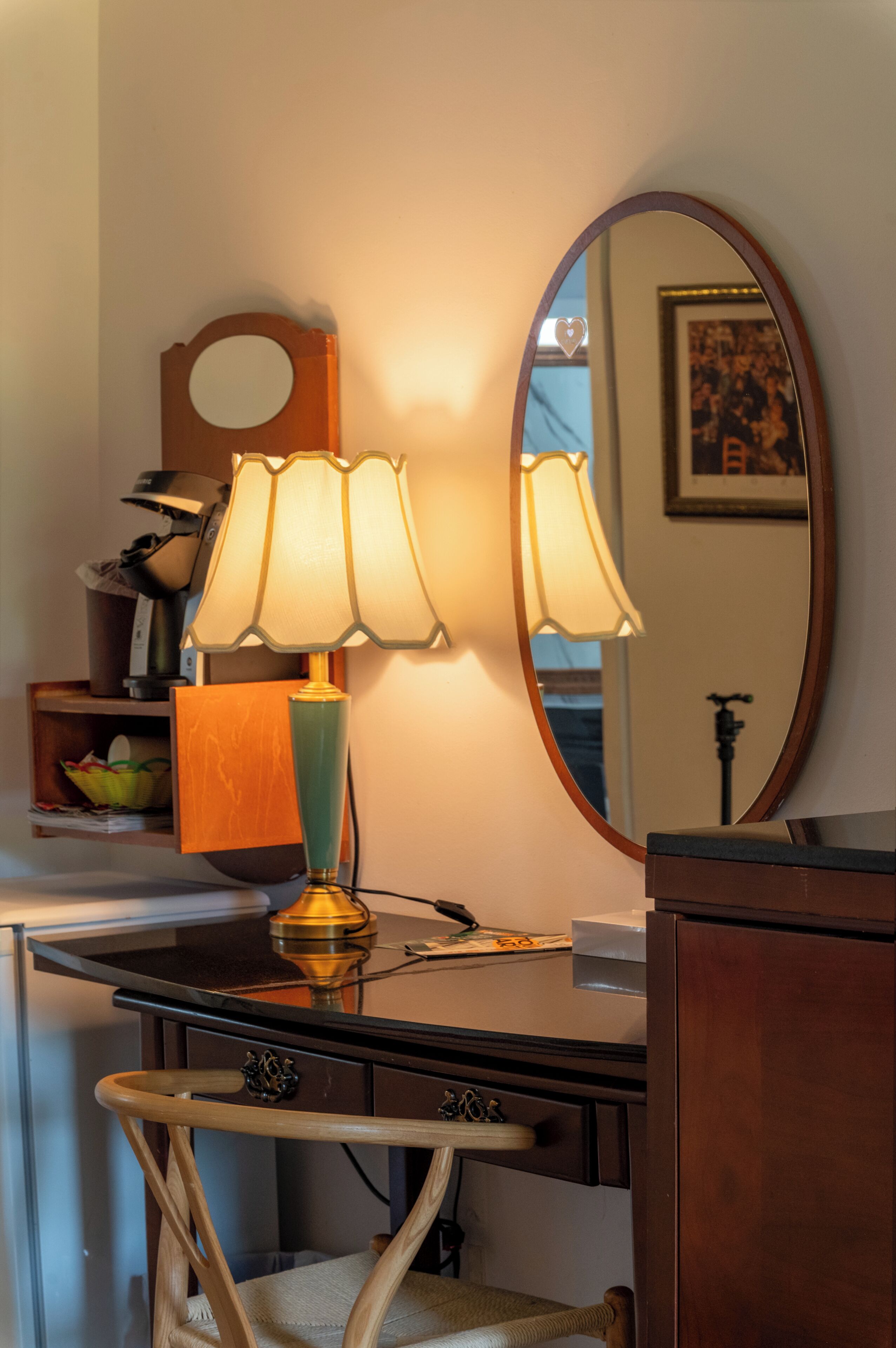A desk with a lamp, a mirror, and a chair.