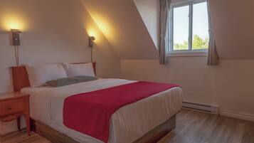 A bedroom with a bed, nightstands, a red blanket, a window with curtains, and wall-mounted lights.