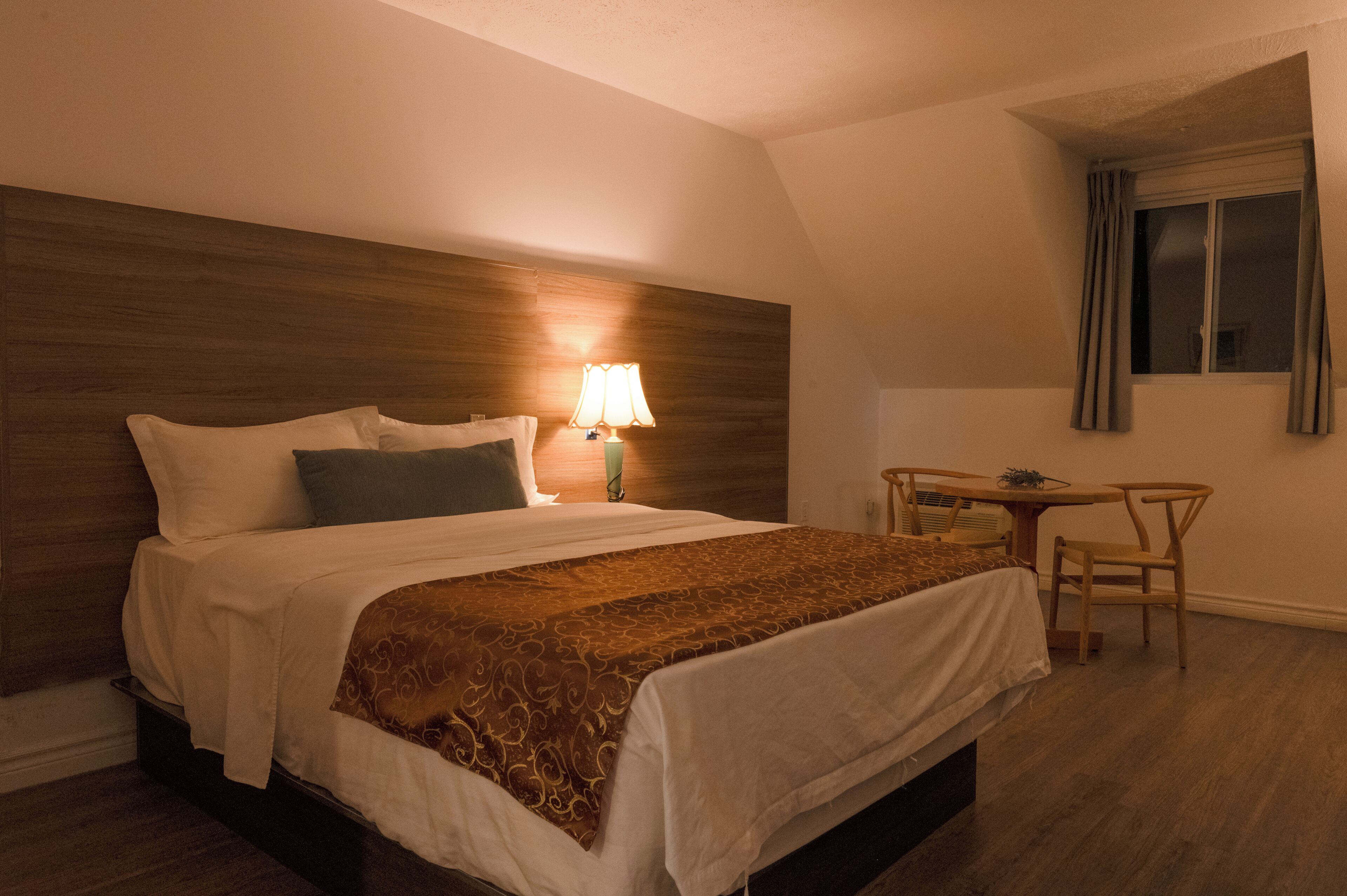 Een hotelkamer met een bed, bedlampje, een klein tafeltje en een stoel.