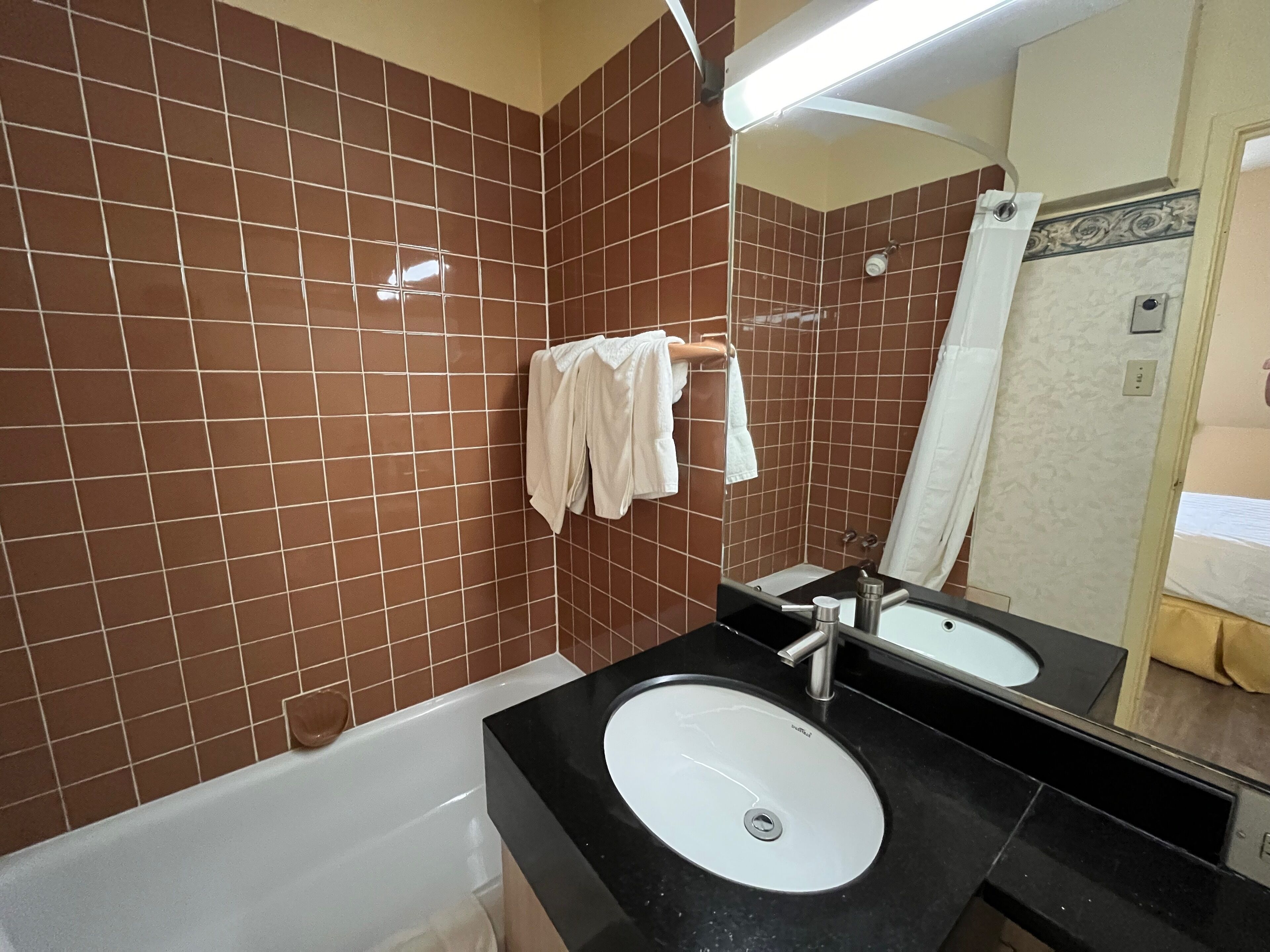 A bathroom with brown tiled walls, a white bathtub, a black sink, and a mirror.