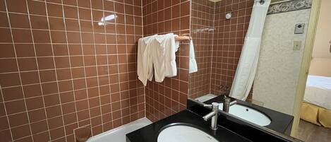 A bathroom with brown tiled walls, a white bathtub, a black sink, and a mirror.