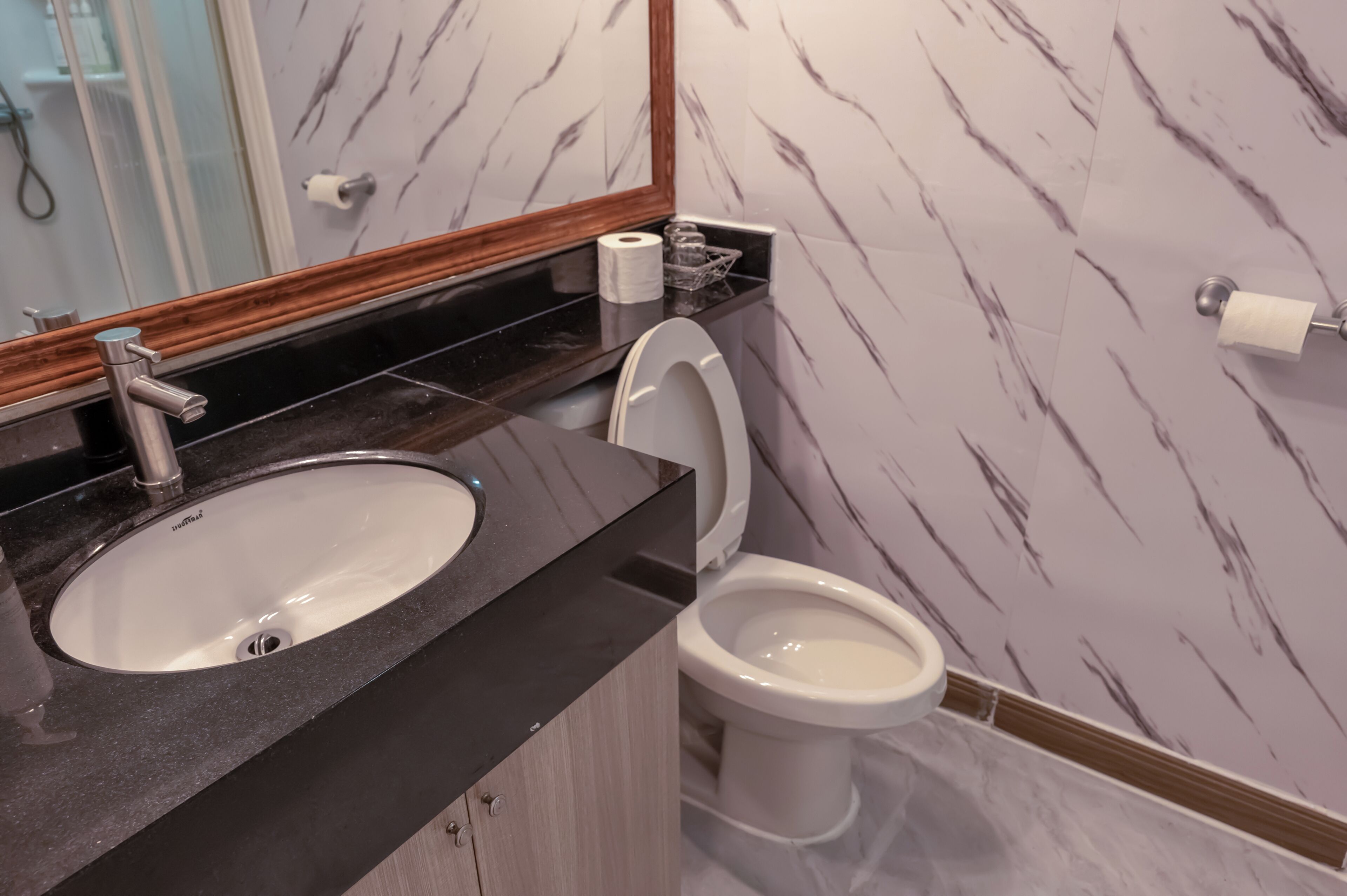 A bathroom with a marble wall, a sink, a toilet, and a mirror.