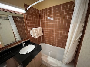 Un baño con encimera negra, lavamanos blanco y bañera.