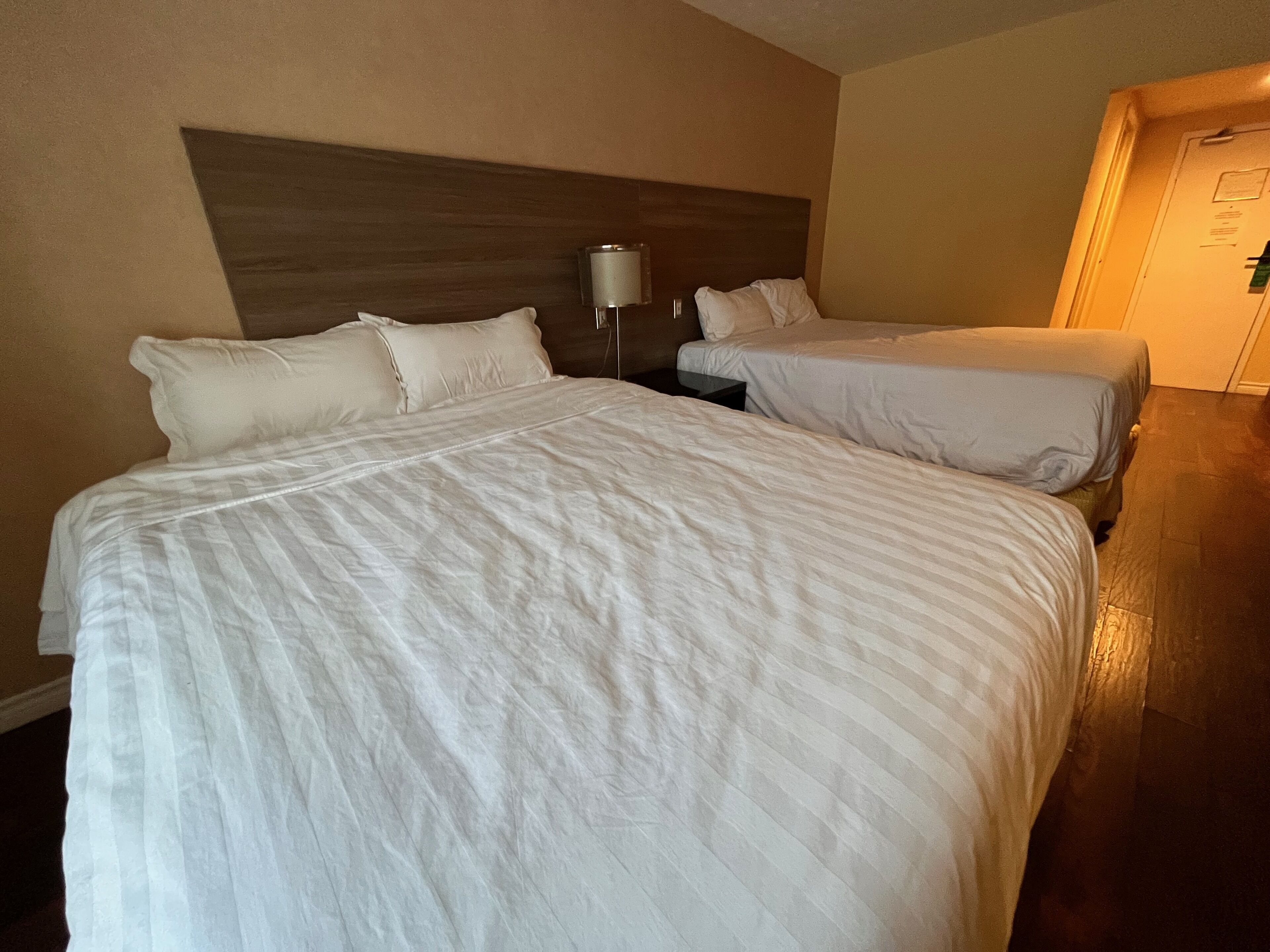 Habitación de hotel con dos camas, una mesita de noche y una lámpara.