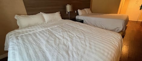 A hotel room with two beds, a nightstand, and a lamp.