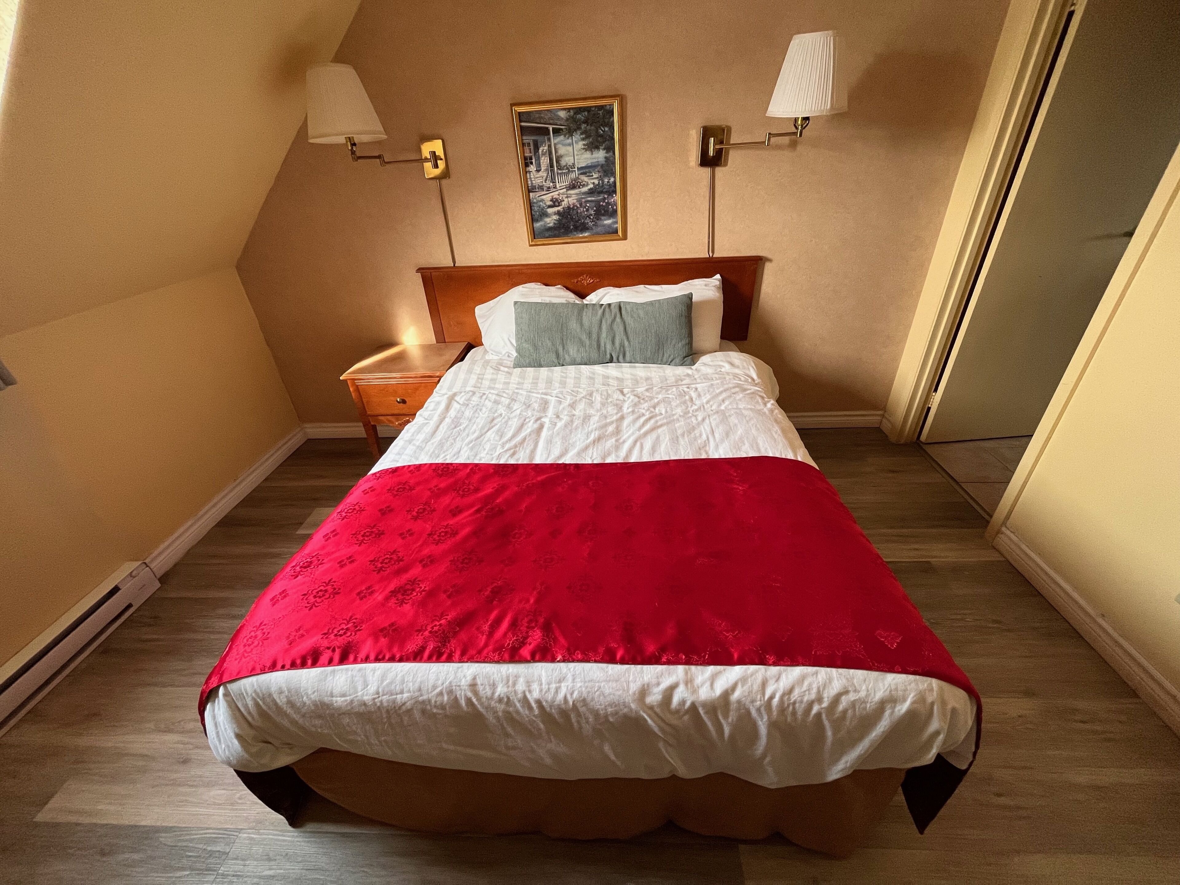 Una cama bien hecha con una colcha roja y blanca, un cabecero de madera y dos lámparas de noche.