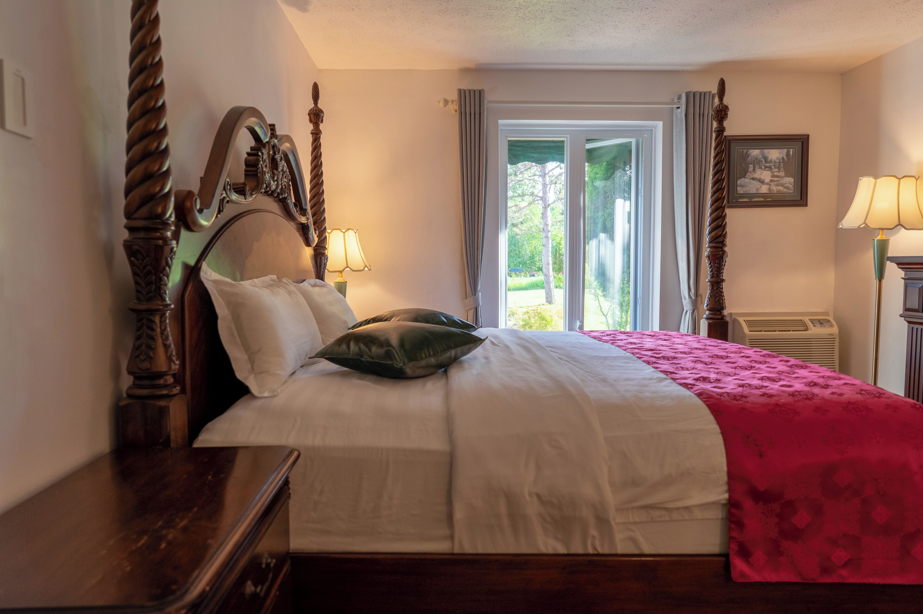 A neatly made bed with a headboard, a bedside table, a lamp, and a window with curtains.