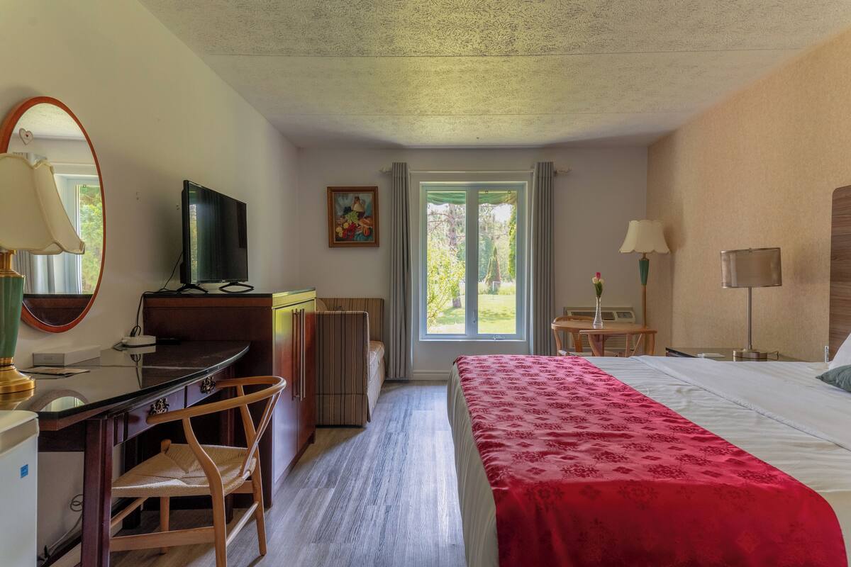 Habitación de hotel con cama, escritorio, silla, televisor y ventana con cortinas.