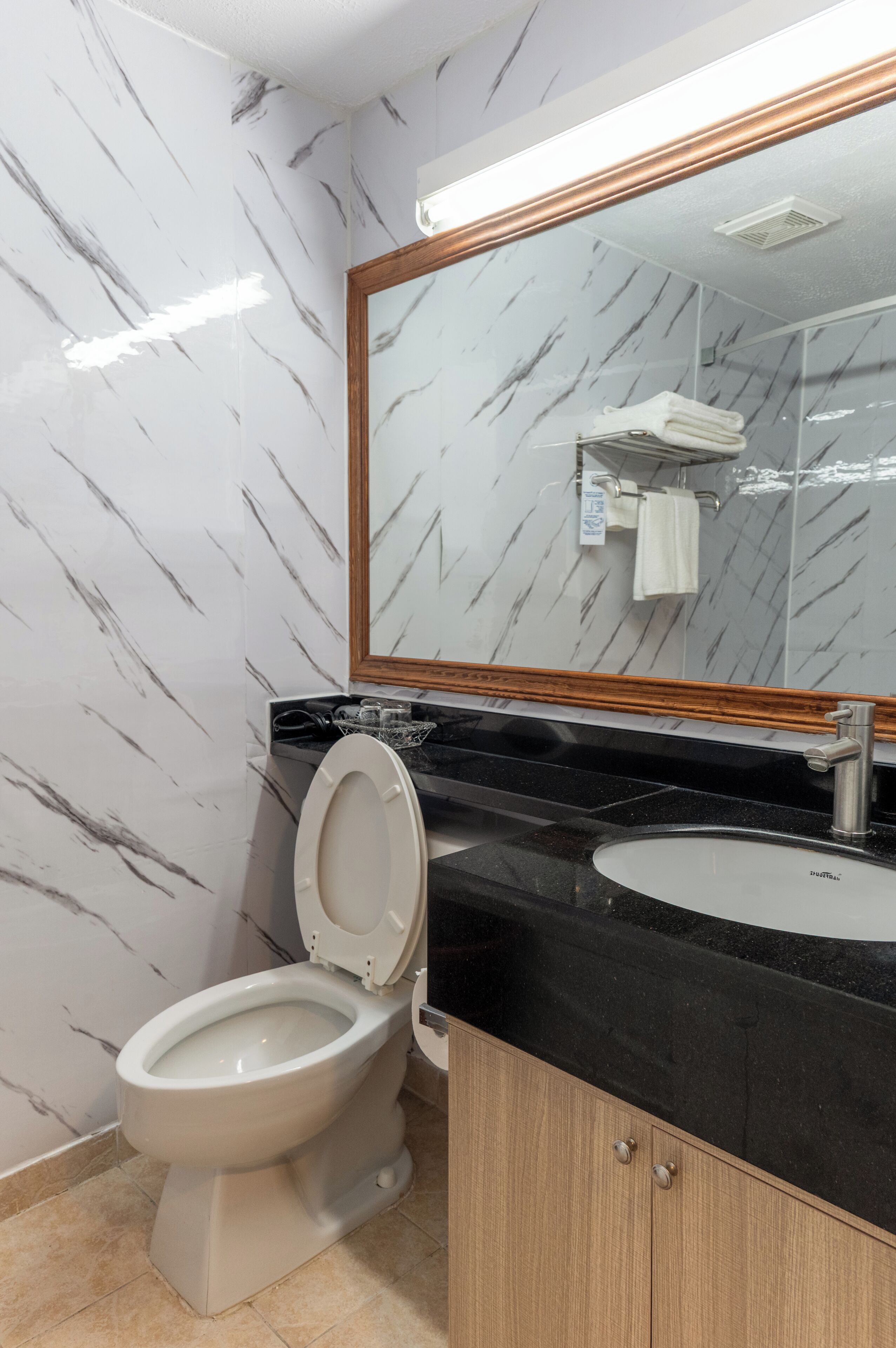 A bathroom with a toilet, sink, mirror, and marble-patterned walls.