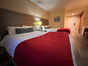 Habitación de hotel con dos camas, cabecera de madera, un escritorio y una lámpara.