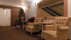 A living room with a Christmas tree, two armchairs, a small table, and a staircase in the background. - Hotel Cowansville (Cowansville)