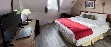 Une chambre d’hôtel avec un lit, un bureau avec un ordinateur portable, une chaise, une télévision, une lampe et une fenêtre avec des rideaux.