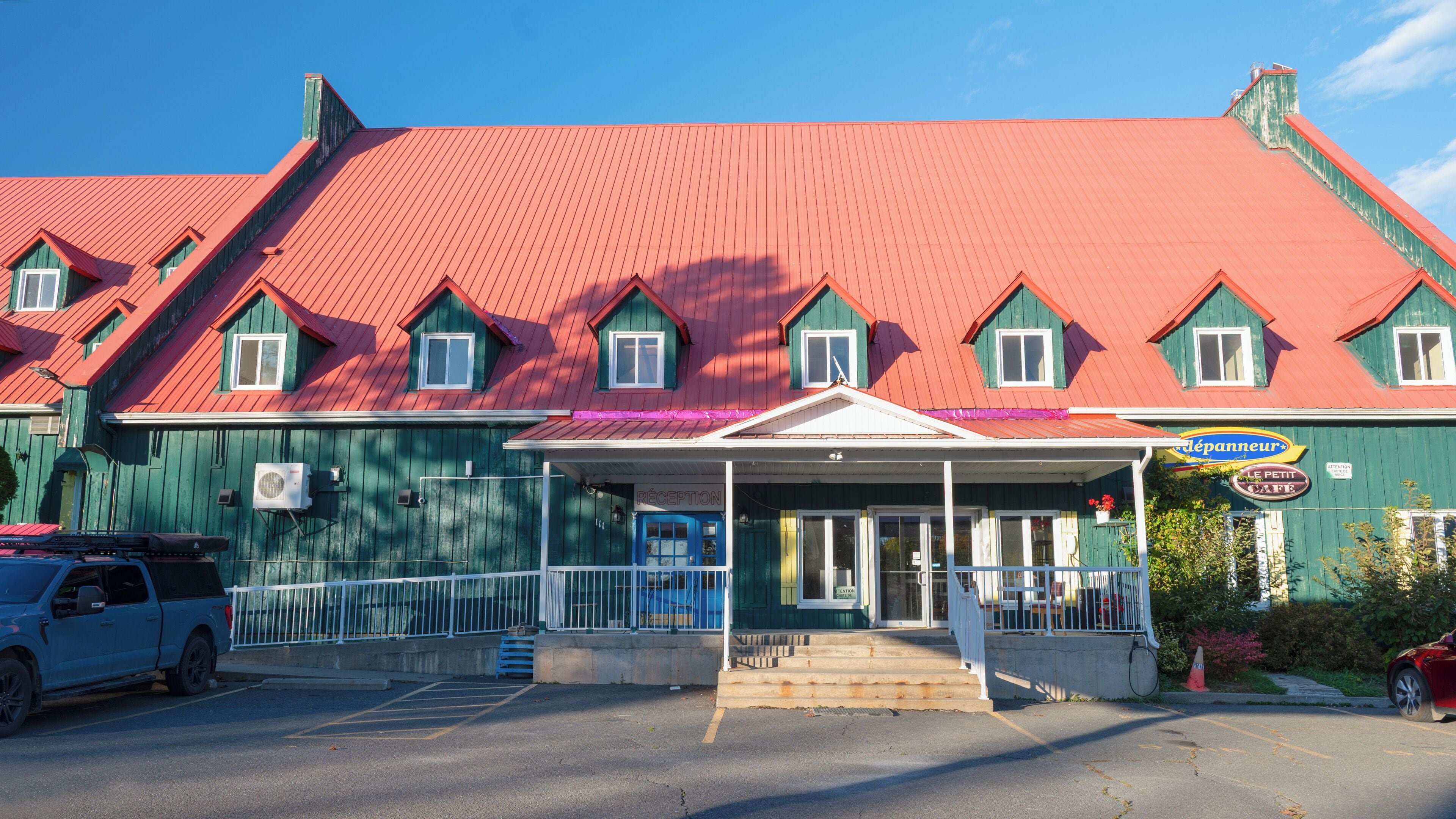 A building with a red roof, a blue entrance, and a sign for 'Le Petit Café'.