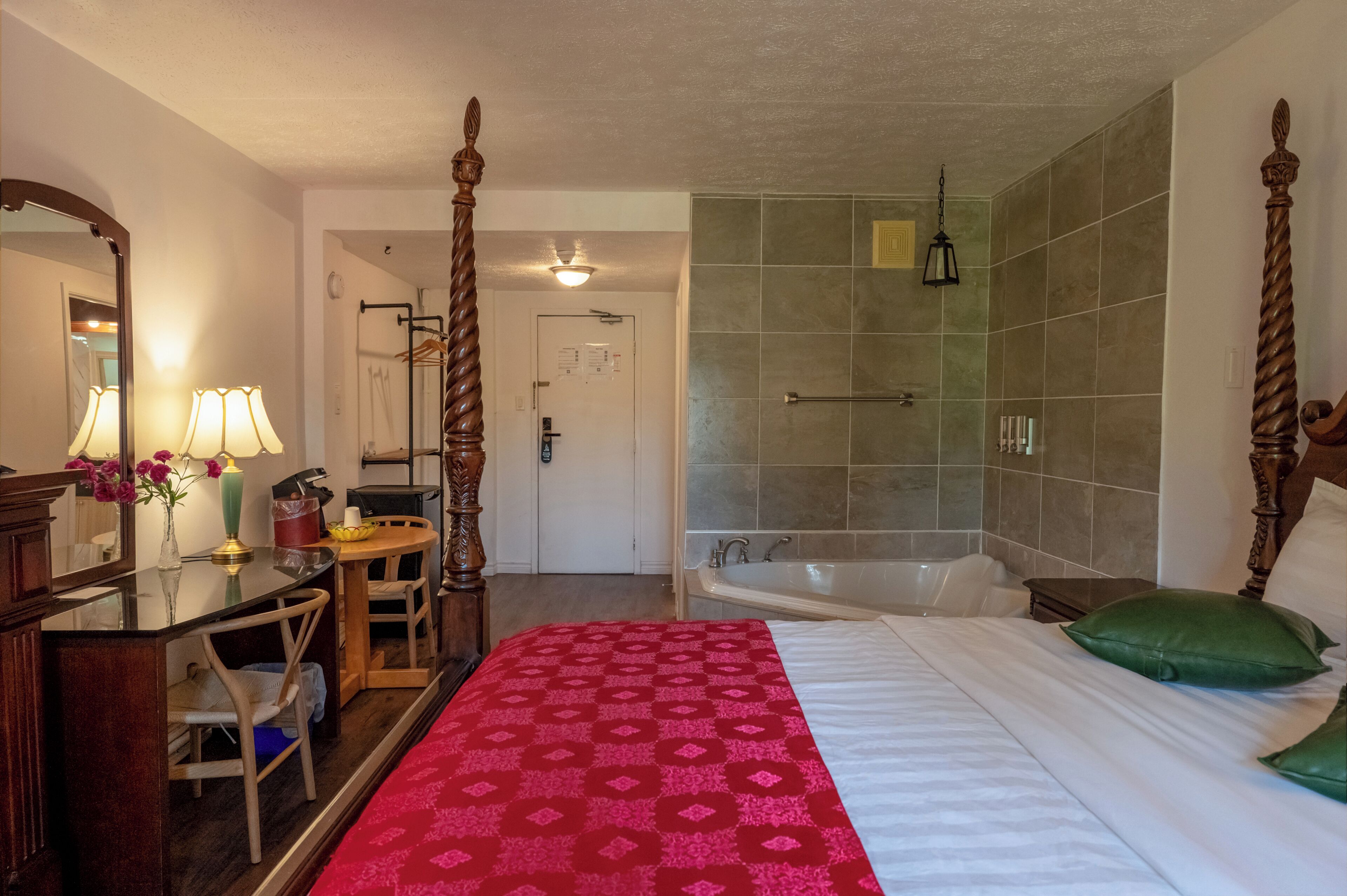 Una camera d'albergo con un letto grande, una zona relax con scrivania e poltrona, un angolo trucco con specchio e un bagno con vasca e doccia.