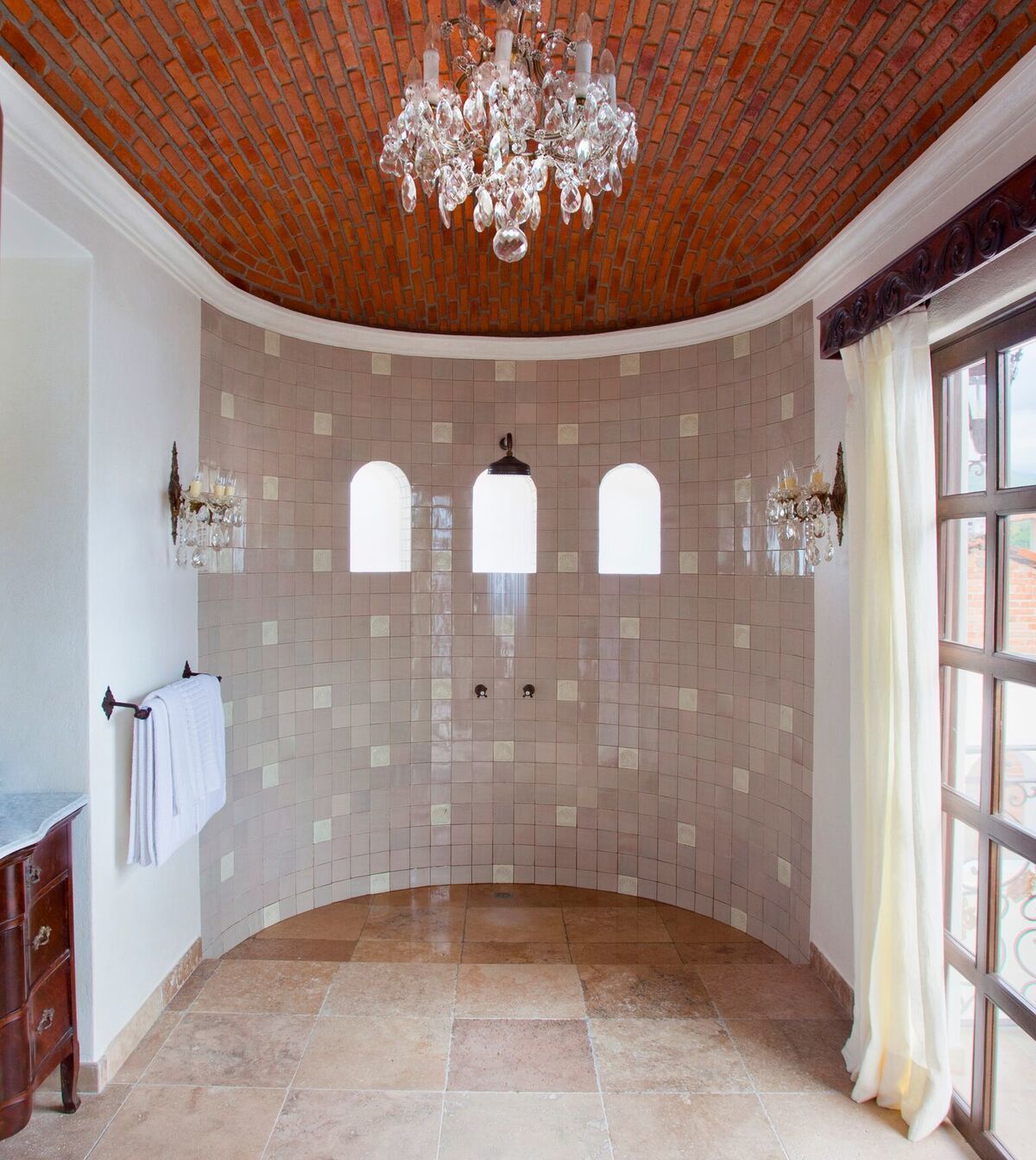 A spacious bathroom with a curved floor, a brick ceiling, and a large chandelier.