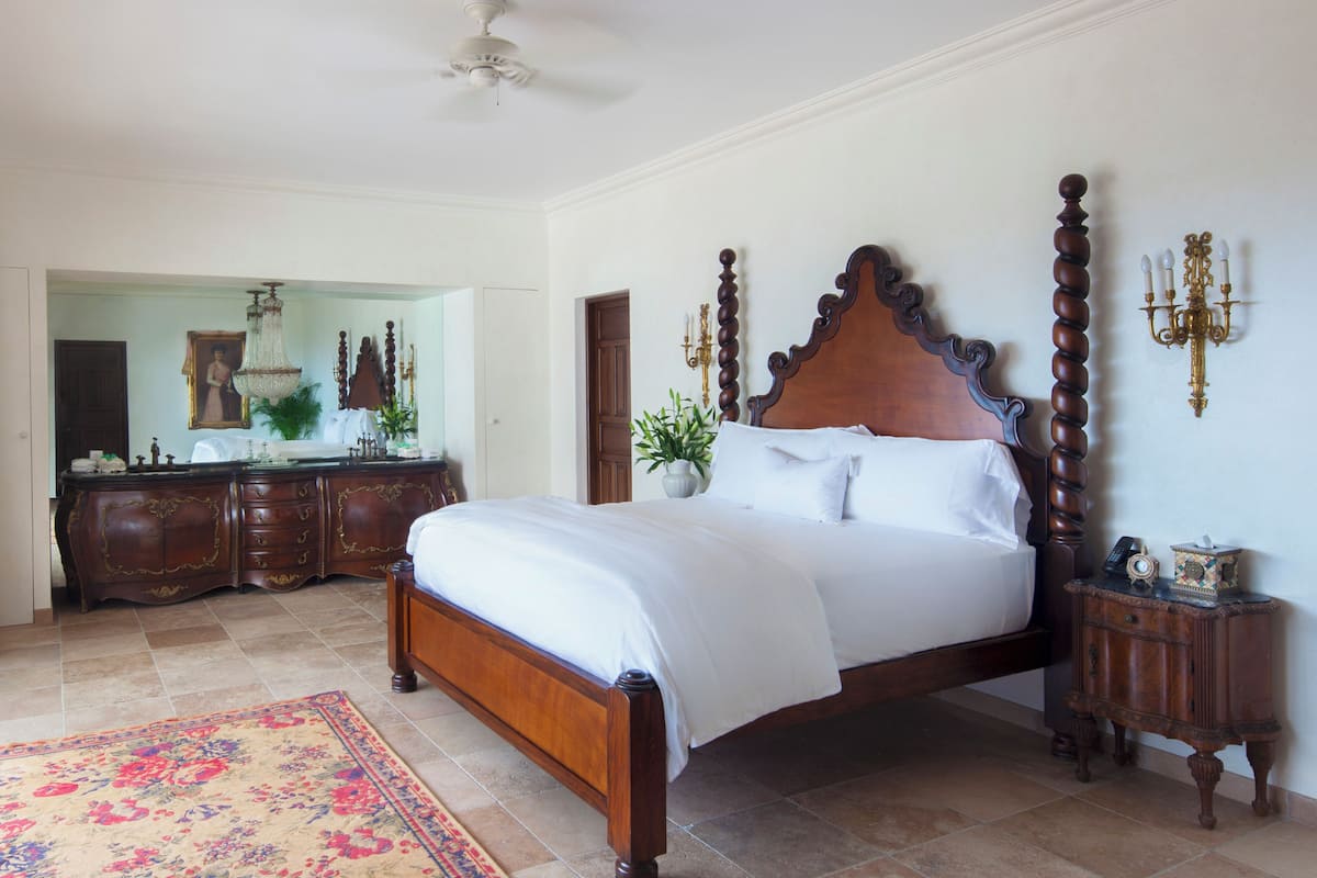 A bedroom with a large bed, a dresser, a mirror, and a chandelier.