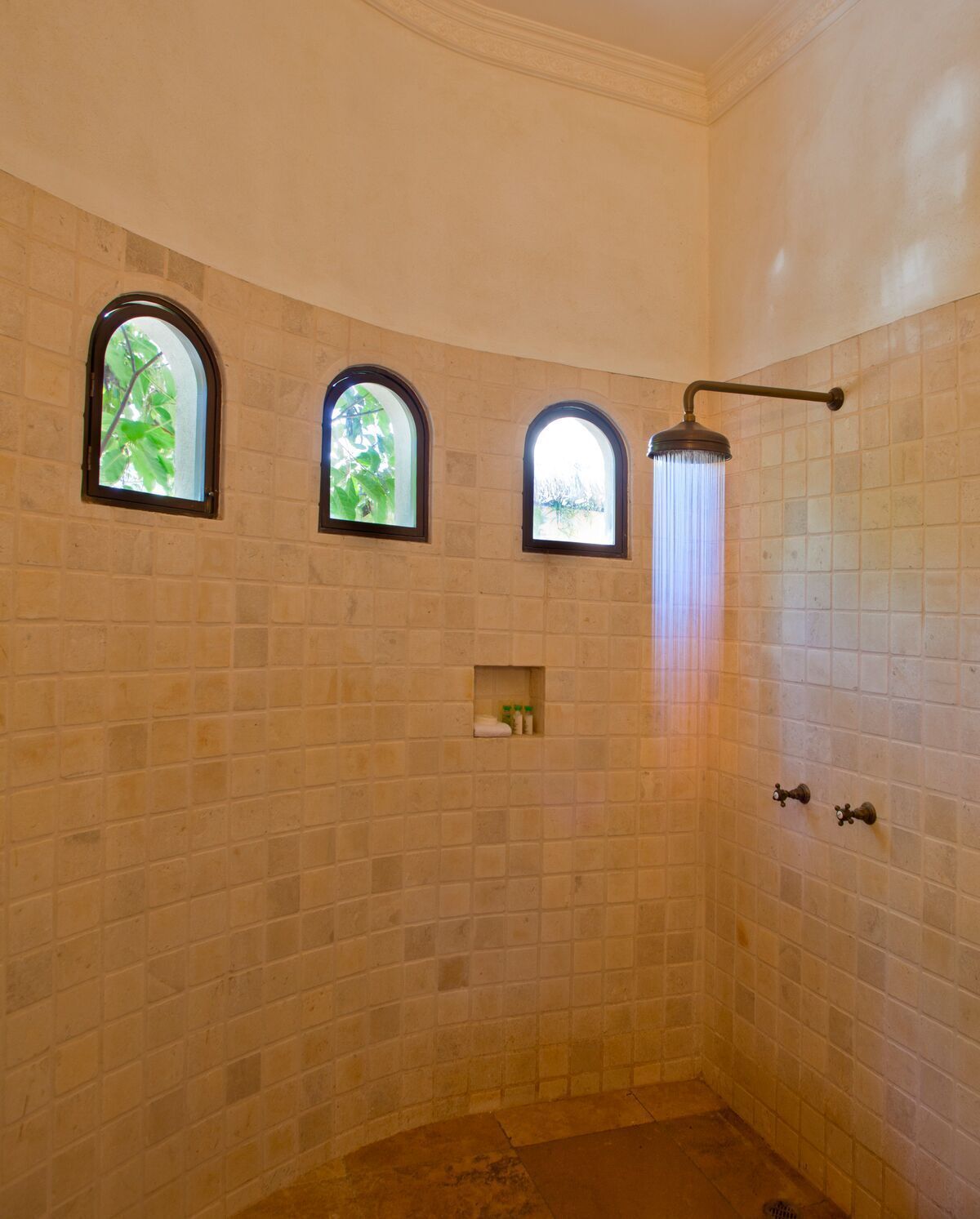 Un baño con tres ventanas de arco, un cabezal de ducha y paredes de azulejos.