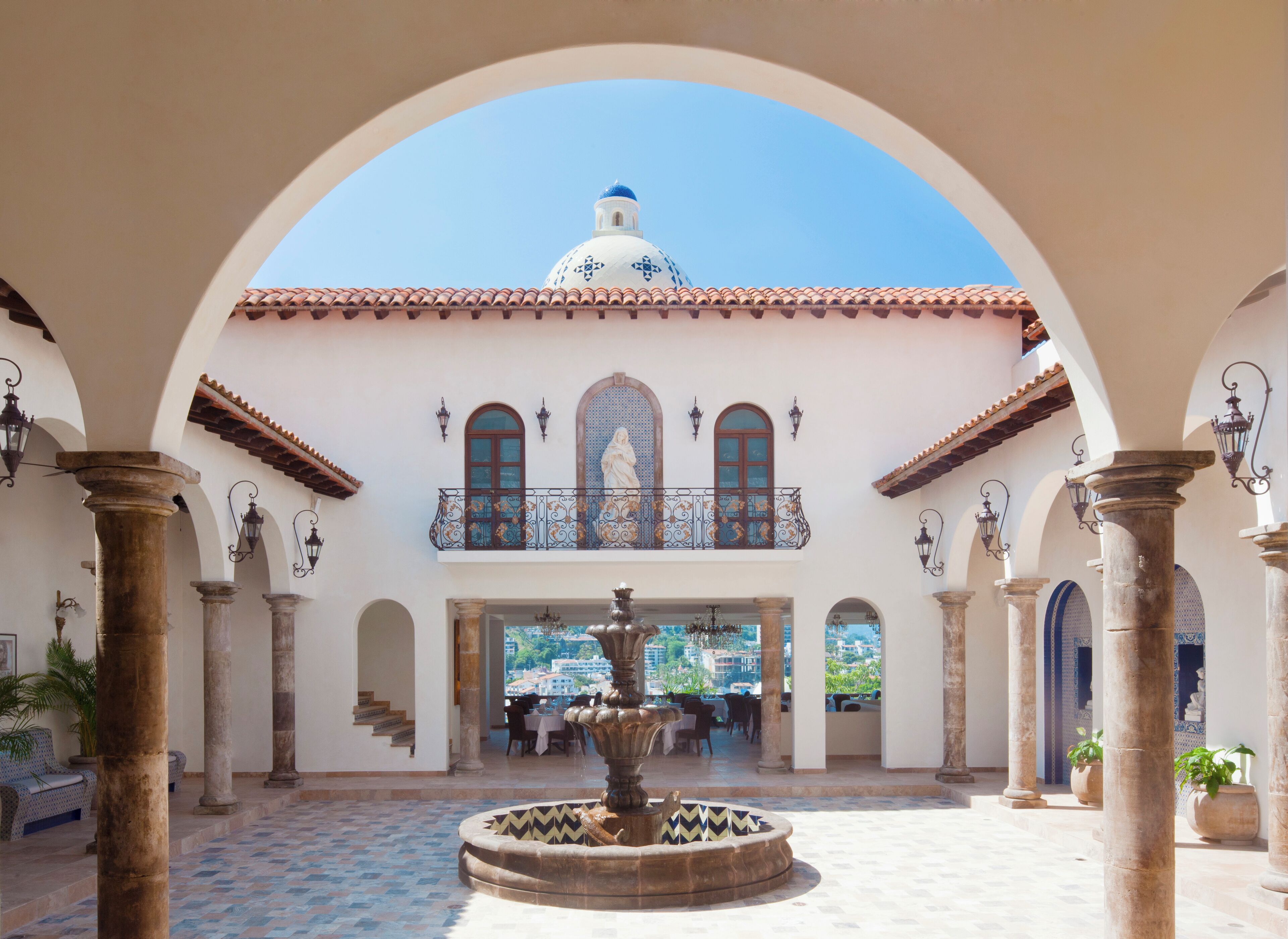 A courtyard with a fountain, columns, and a balcony with a statue.