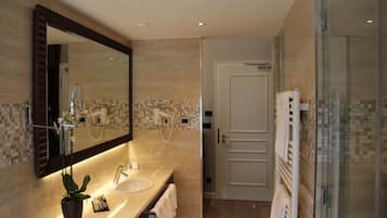 A modern bathroom with a large mirror, a sink, a potted plant, and a glass shower enclosure.
