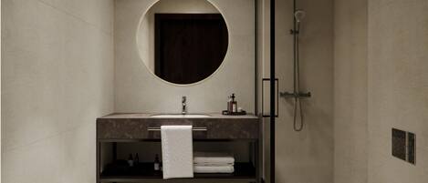 Un baño moderno con un espejo redondo, un lavabo, una ducha y un inodoro.