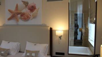 A hotel room with a bed, a wall-mounted lamp, a large window, and a framed picture of seashells.