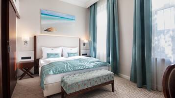 Habitación de hotel con una cama grande, una mesita de noche, un banco, un cuadro de playa y vistas al exterior por la ventana.