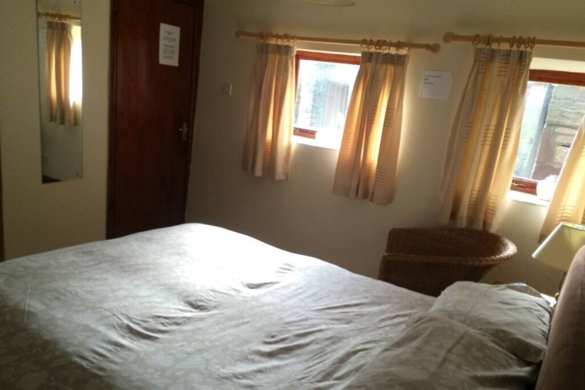 Quarto com cama, cadeira, janela com cortinas e porta.